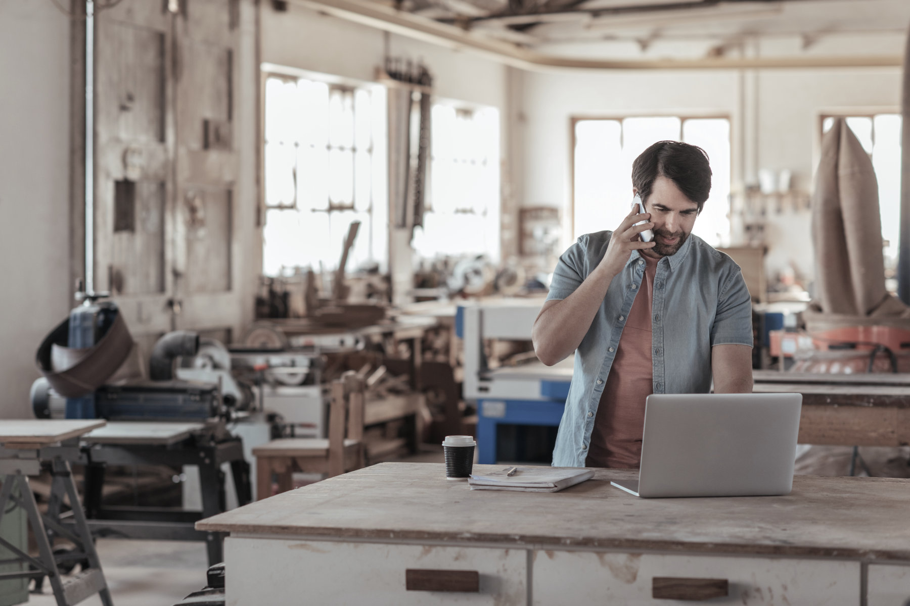 Commercial Property Insurance - A man in a workshop talking on a cell phone and using a laptop computer.