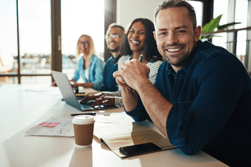 Employee Benefits in MN - Four employees seated at a desk smiling.