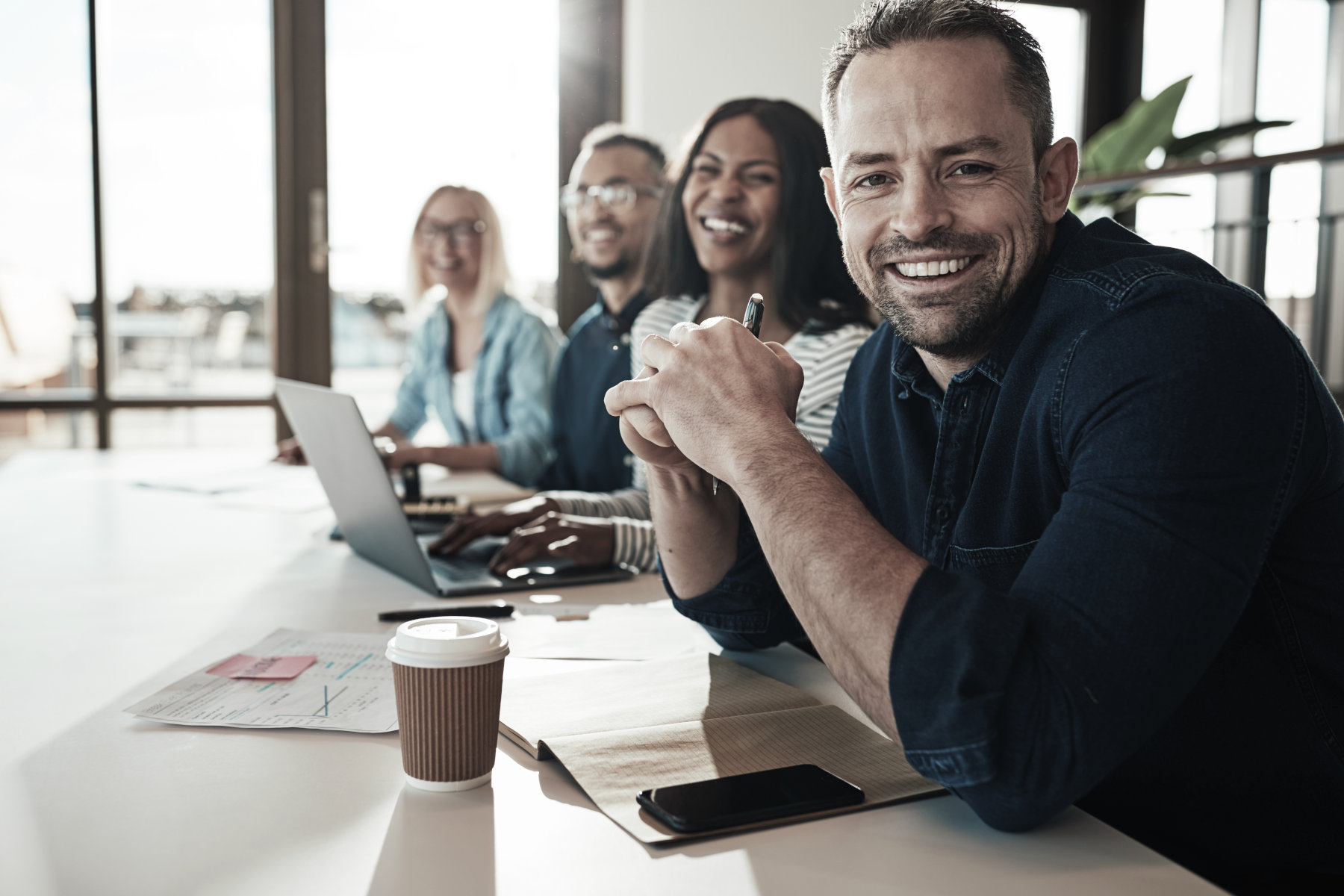 Employee Benefits - Four employees seated at a desk smiling.