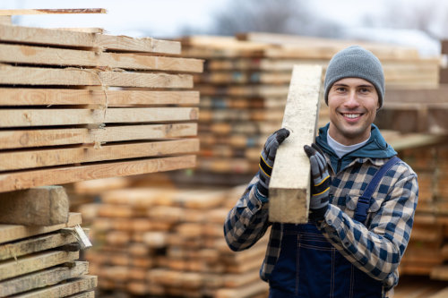 Workers Compensation Insurance in MN - A man in overalls and a hat holding a board over his shoulder.